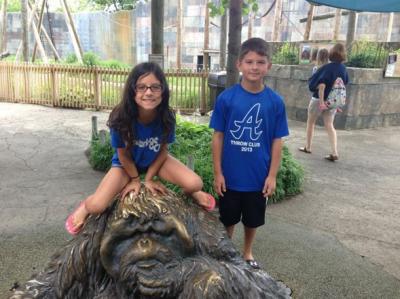 a girl sitting on a statue of an orangatang and a boy standing next to her