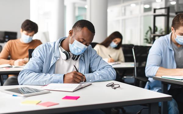 students sitting at desks writing while wearing masks